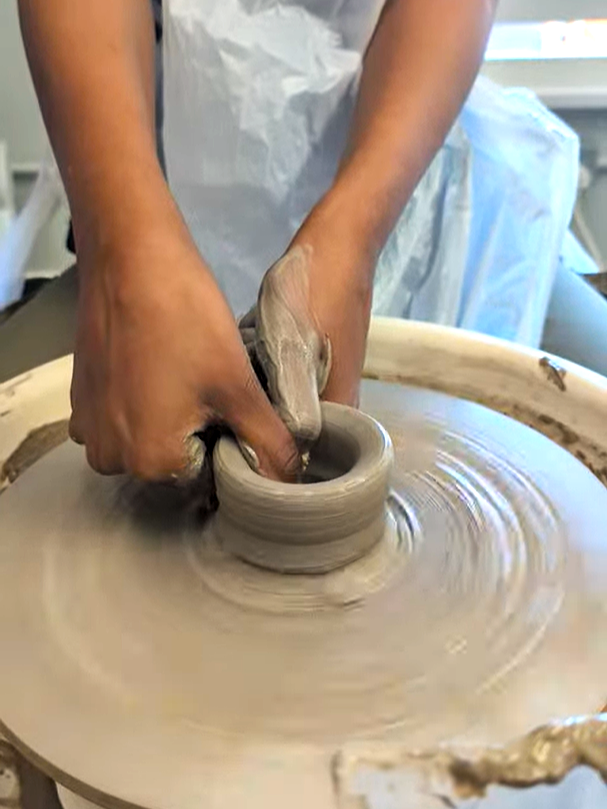 Hands shaping a clay vessel on a spinning potter's wheel