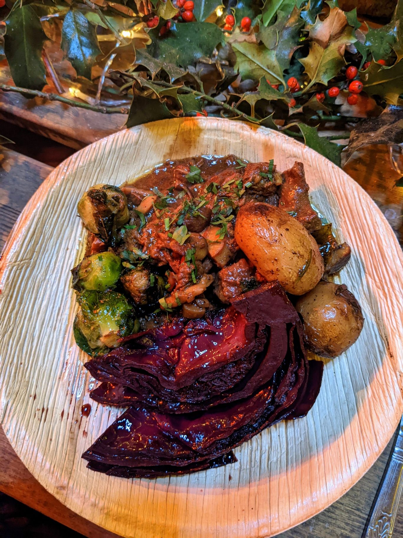 A winter plate of stew, sprouts, roast potatoes and red cabbage beside holly
