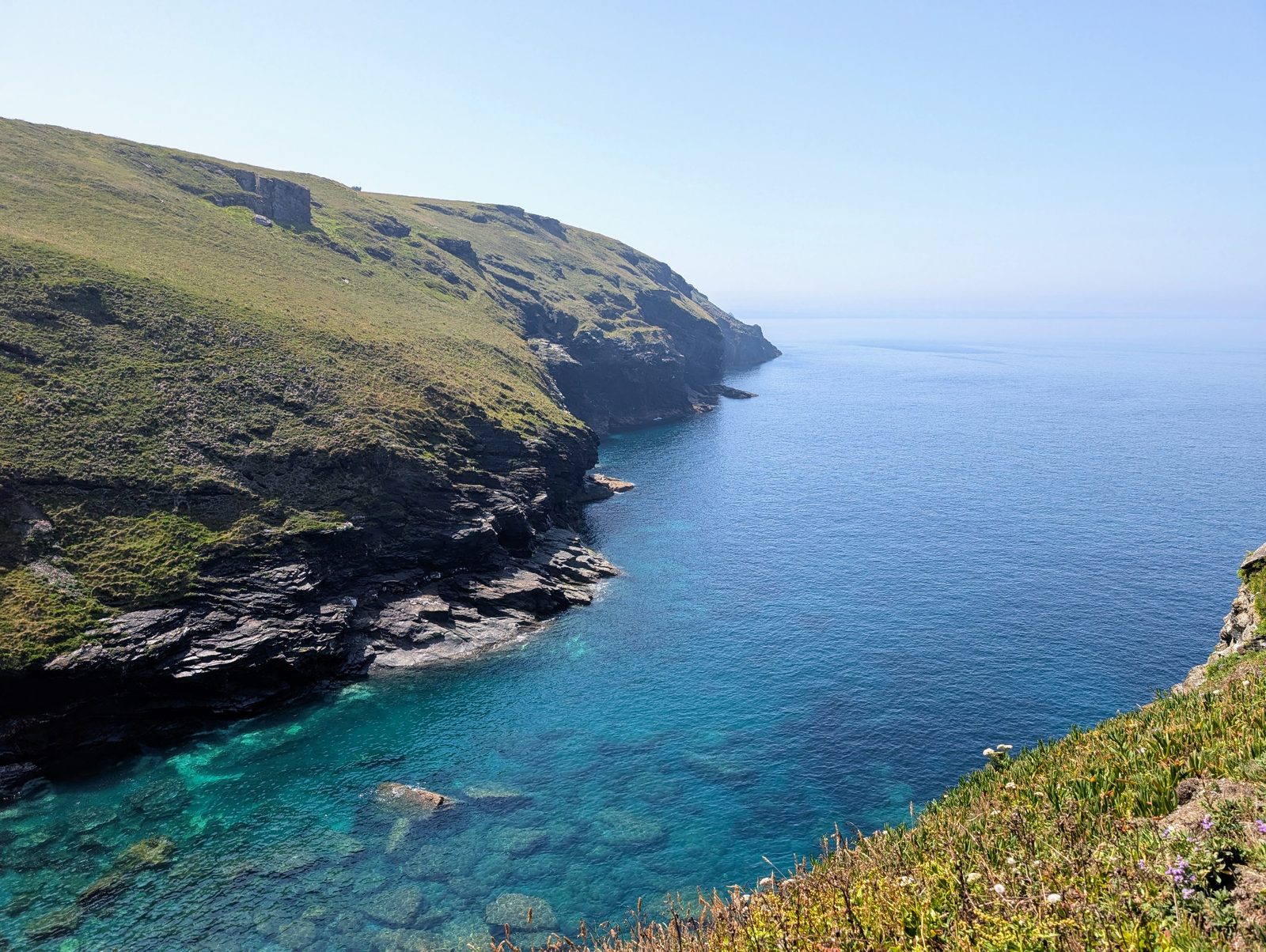 Sunlit Cornish cliffs falling into a clear turquoise cove