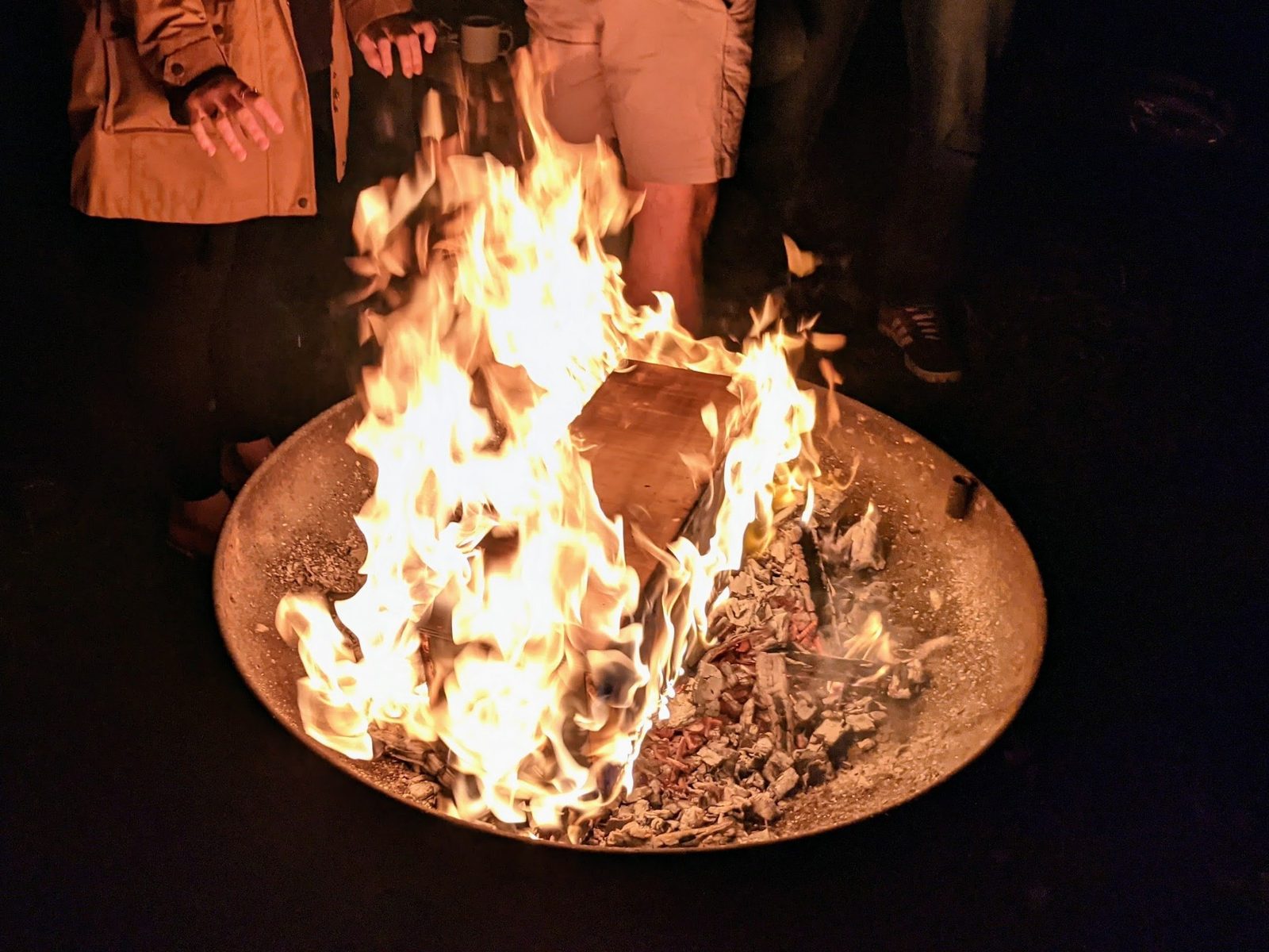 A bonfire burning in a fire pit at night with people gathered around