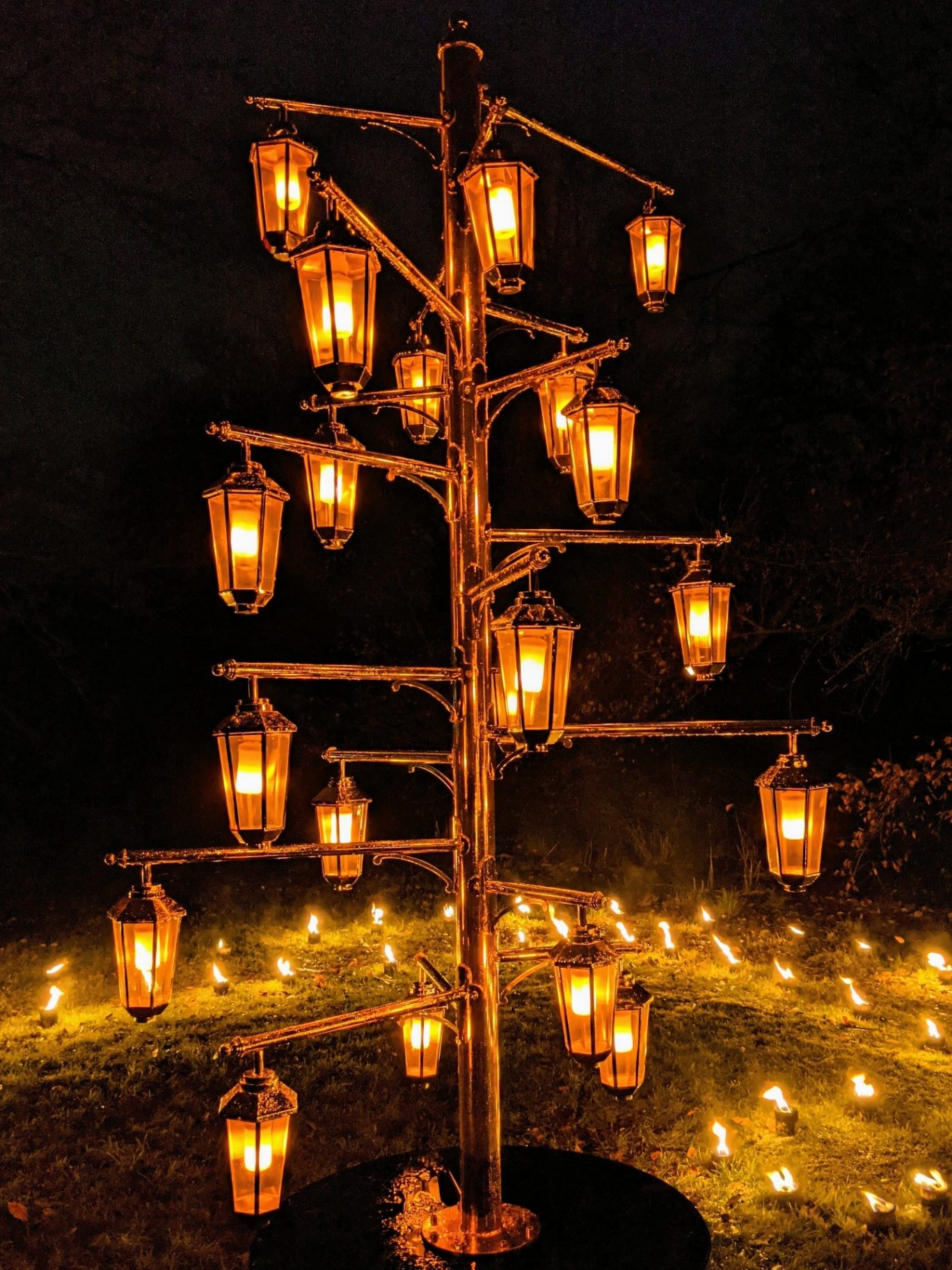 A wrought-iron lantern tree glowing with candles at night