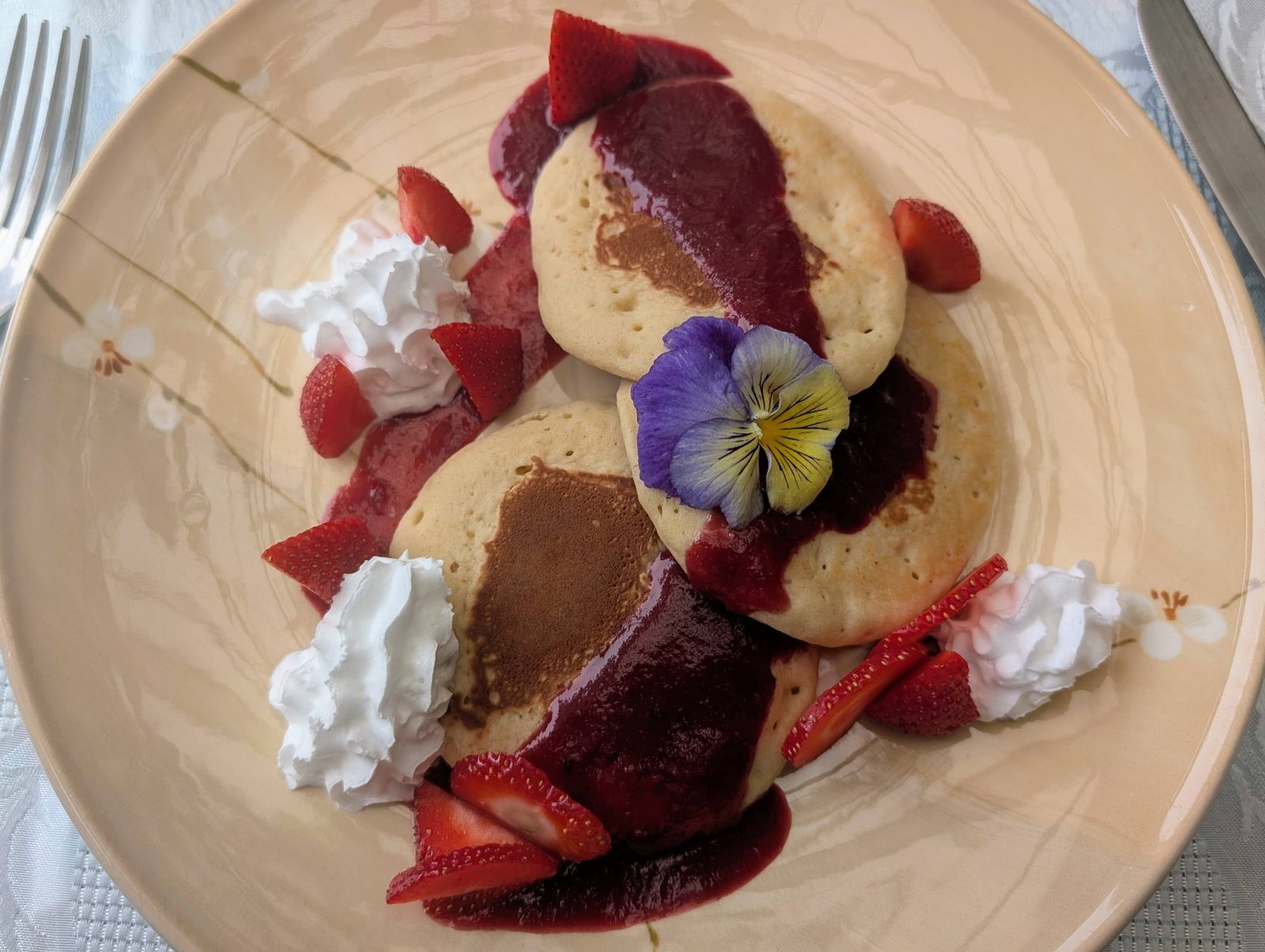 Pancakes with berry coulis, strawberries, cream and an edible pansy