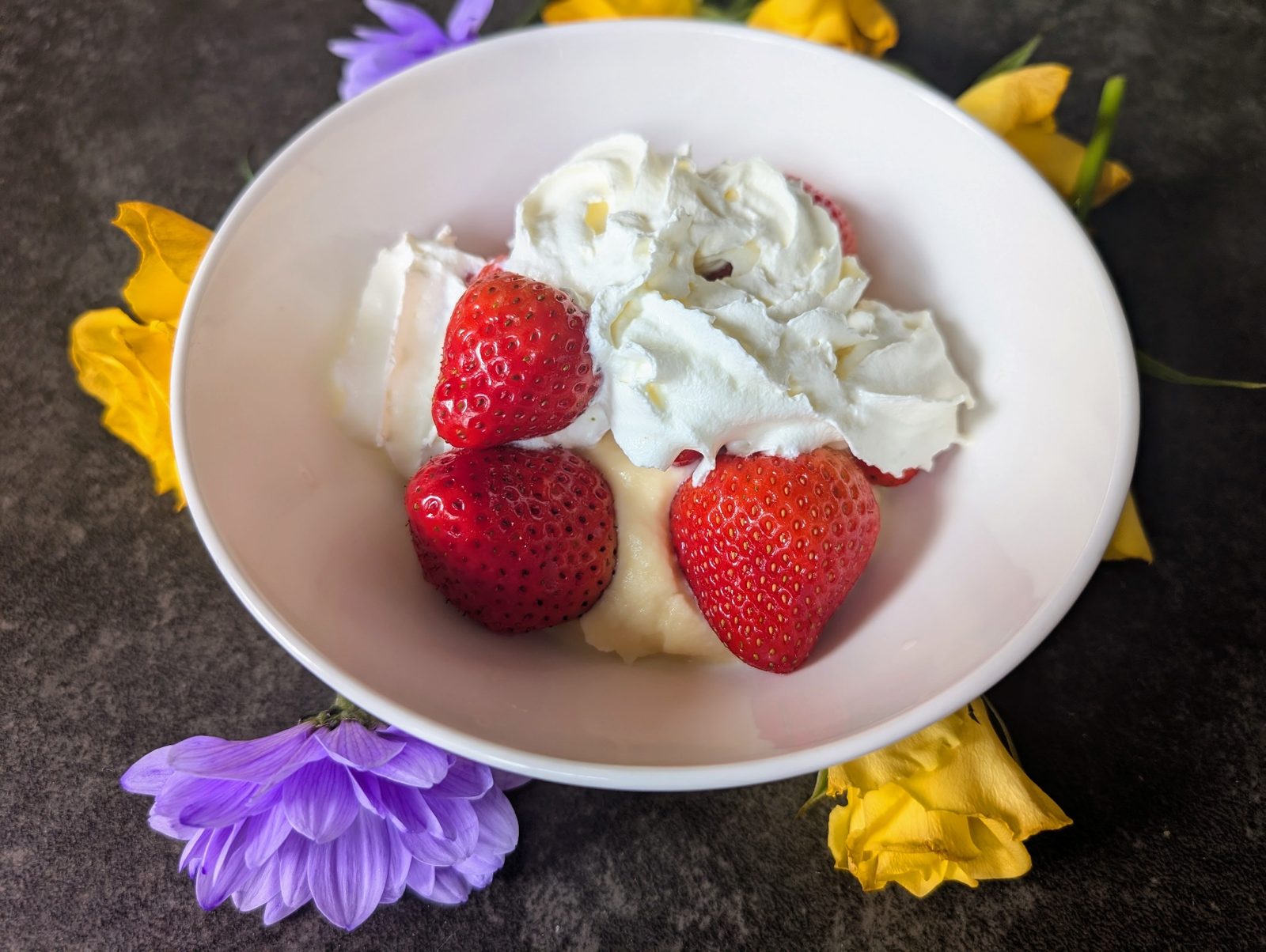 Strawberries and cream in a bowl surrounded by summer flowers