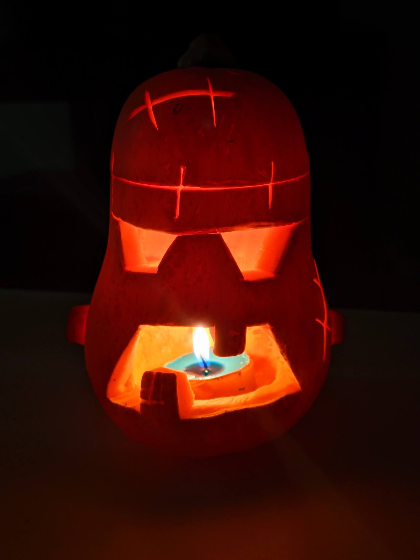 A carved butternut squash jack-o'-lantern lit from within by a candle